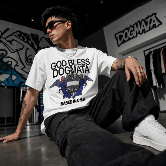 Person wearing a white t-shirt with 'GOD BLESS DOGMATA' text and graphics, sitting in a store.