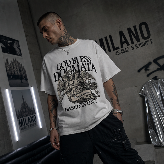 Model wearing a white t-shirt with graphic design and text, standing in a room with posters on the wall.