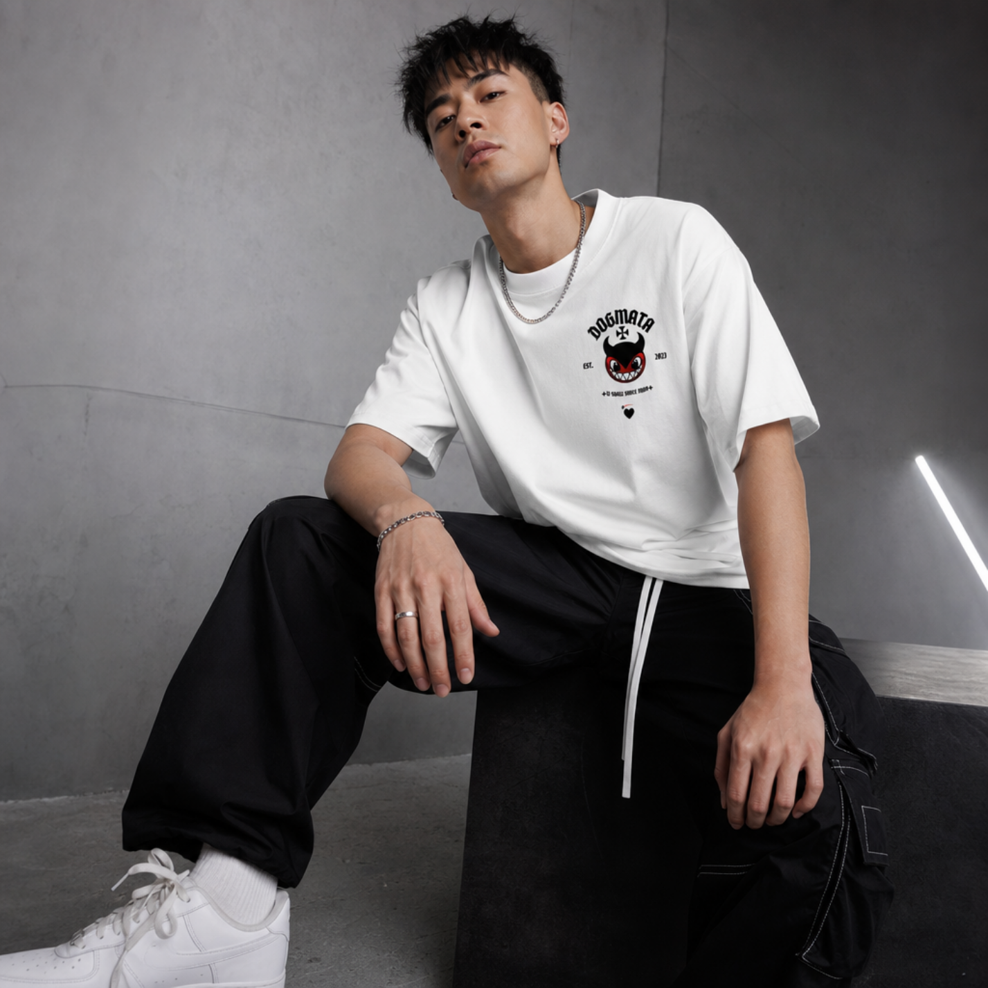 Model wearing a white t-shirt with a graphic design, sitting against a gray background