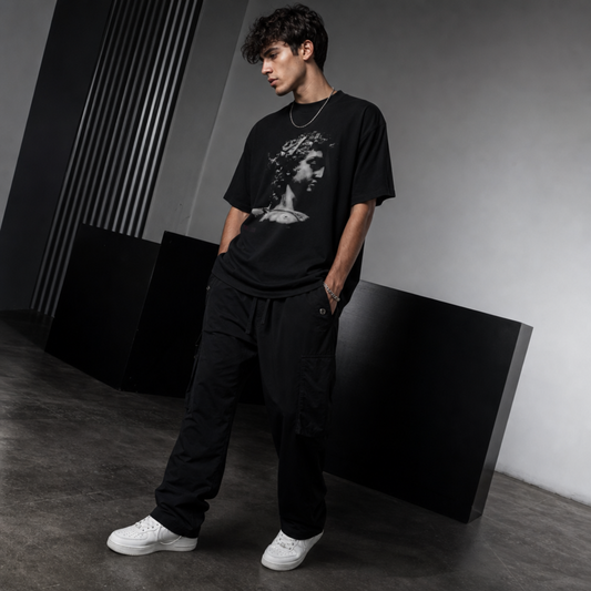 Model wearing a black graphic t-shirt and black pants in a minimalistic setting