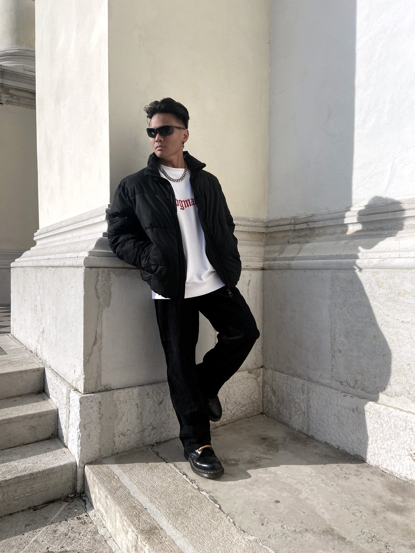 Model wearing a black jacket with a white organic cotton sweatshirt and black pants, standing on steps with hands in their pockets.